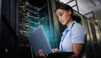 Revolutionize Your IT: Why Smart IT Leaders Are Rethinking Virtualization // Black woman using laptop in data center
